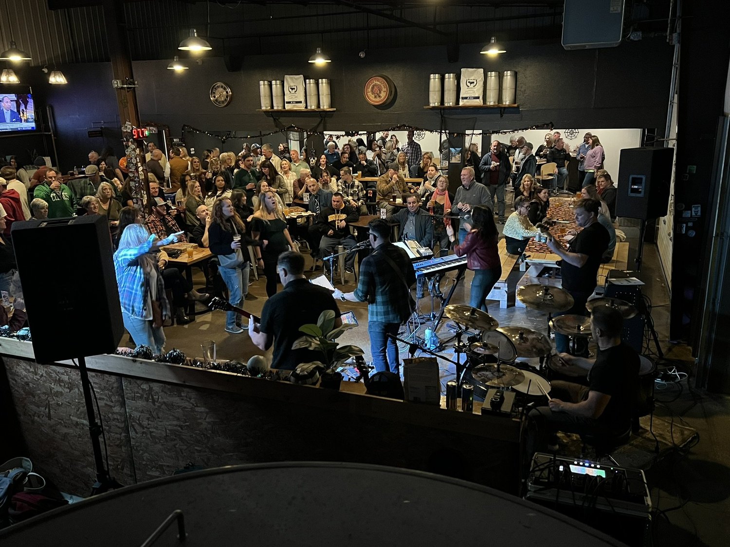 People attending a live music performance in a dimly lit bar or pub, with a band playing on stage and audience members watching and socializing.