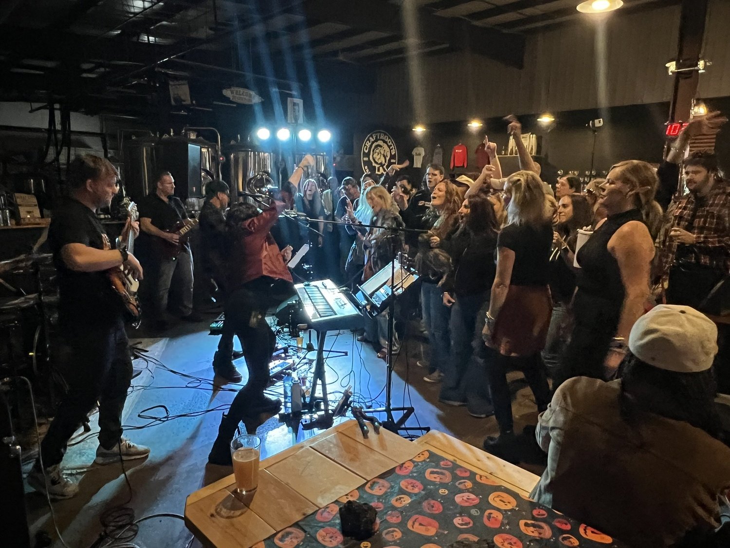 People dancing and enjoying live music performance at a bar or club, with band members playing guitars and keyboard on stage, and blue stage lights illuminating the scene.